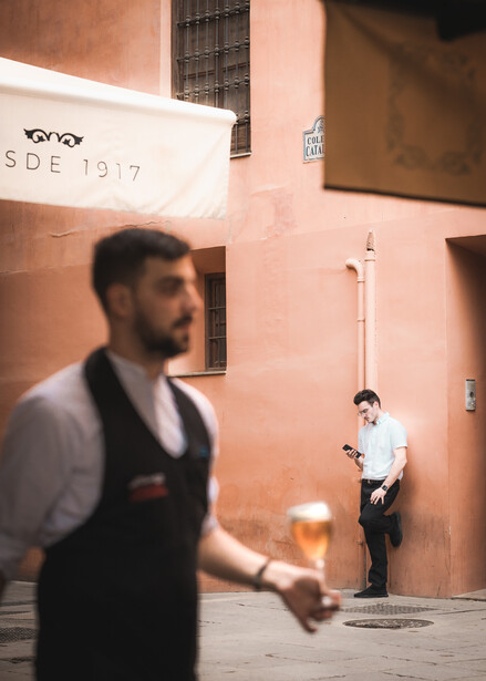 An image showing two members of bar staff in a terrace in Granada, Spain – one takes a rest in the background as the other serves drinks to waiting customers.
