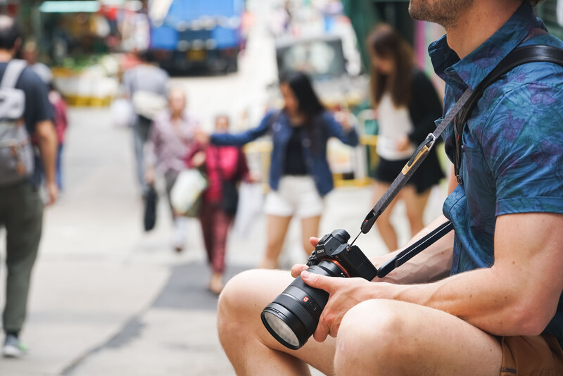 Photographer holding a DSLR camera with telephoto lens at a crowded outdoor street event.