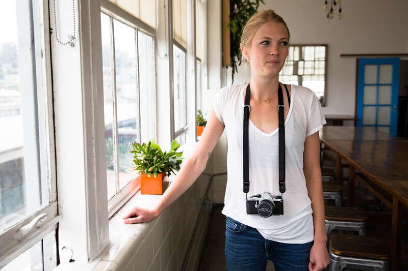 Woman holding potted plant by bright window with vintage camera around neck.