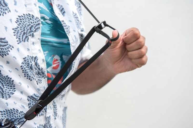 Person's hand holding a camera shoulder strap with black hardware against patterned fabric.