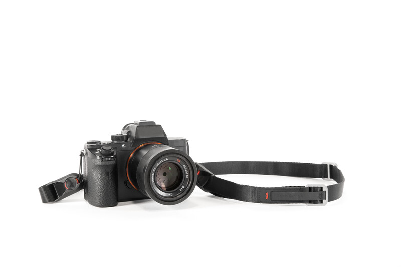 Professional mirrorless camera with attached lens and black shoulder strap displayed on white background.
