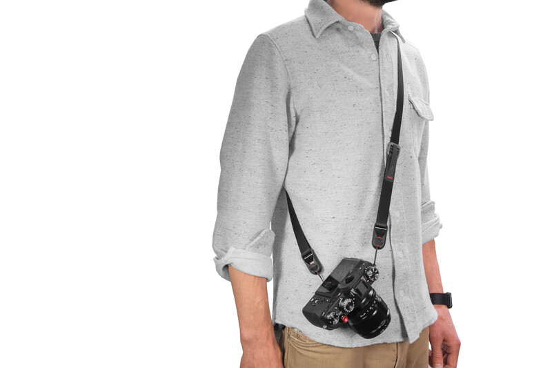 Man wearing gray button-up shirt with camera bag slung across his torso.