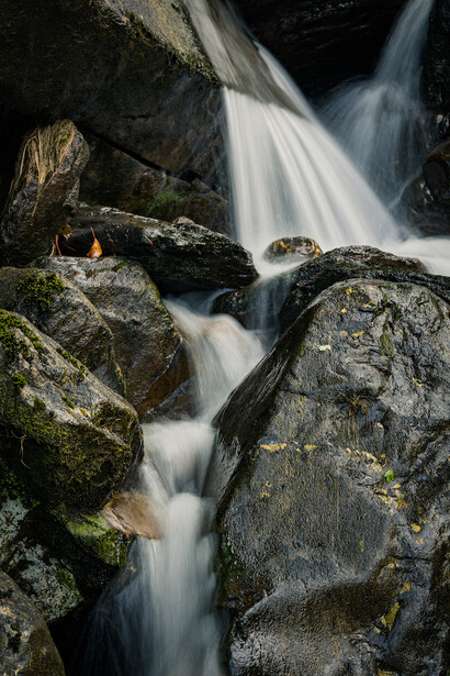 Cascading waterfall flowing between moss-covered boulders with silky water effect.