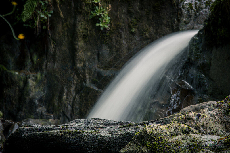 Smooth flowing waterfall cascading through moss-covered rocky canyon with a fallen log in the foreground.