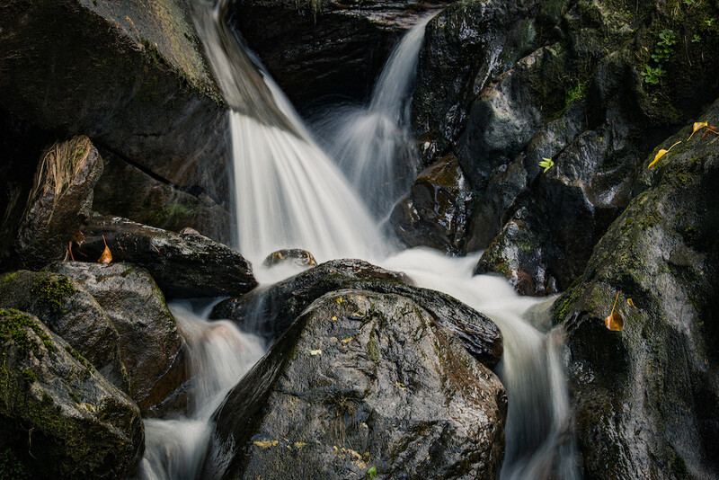 Silky waterfall cascading over moss-covered boulders in a rocky stream gorge.