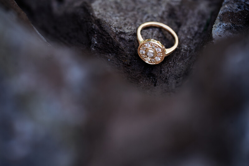 Gold engagement ring with round diamond center stone on dark textured surface.