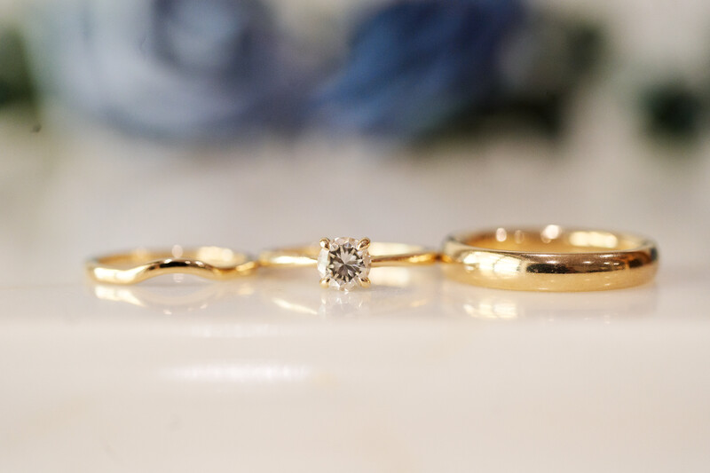 Two gold wedding bands with a round diamond solitaire engagement ring displayed on white marble surface.