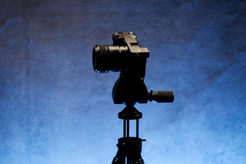 Camera with telephoto lens mounted on tripod head silhouetted against blue sky.