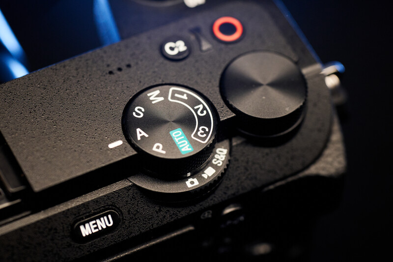 Close-up of camera mode dial showing aperture priority setting with manual focus ring visible.
