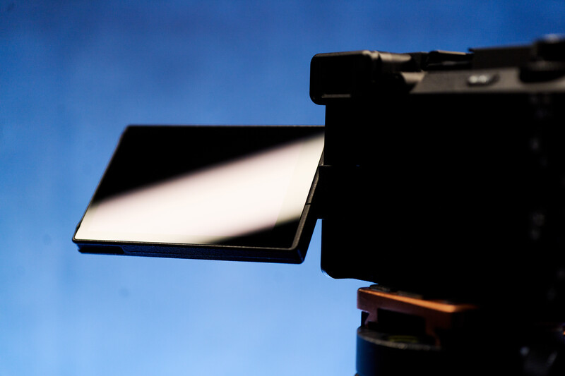 Flash unit with white diffuser panel mounted on camera against blue sky.