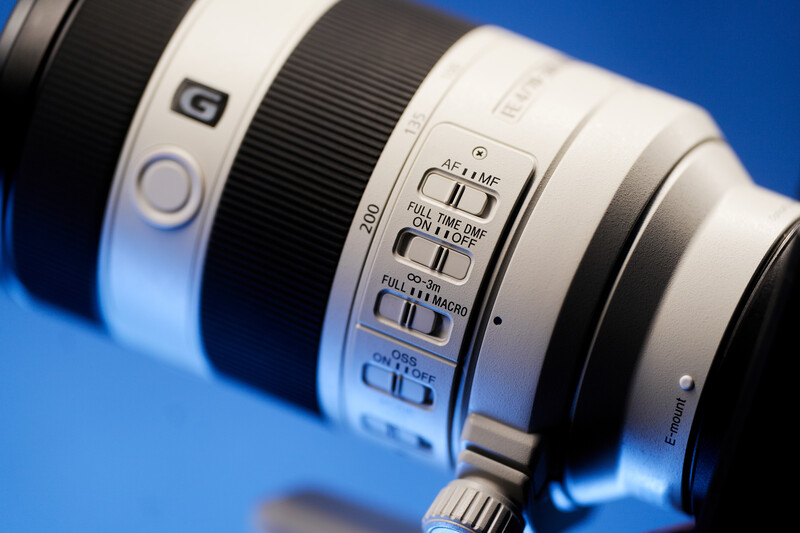 Close-up of a white telephoto lens barrel showing focus and image stabilization controls against a blue background.