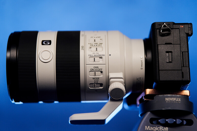 White telephoto zoom lens with focus and aperture rings mounted on a camera body against blue background.