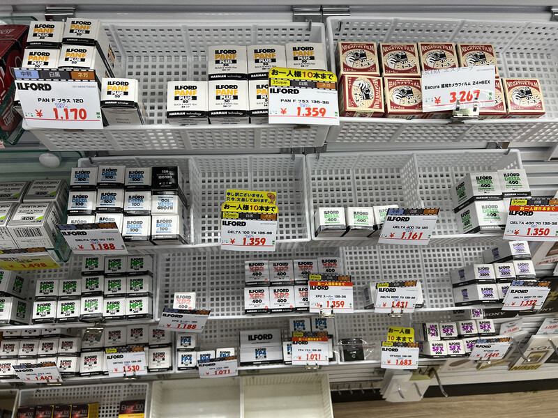 Photography film and camera equipment displayed on retail shelves with Japanese price tags.