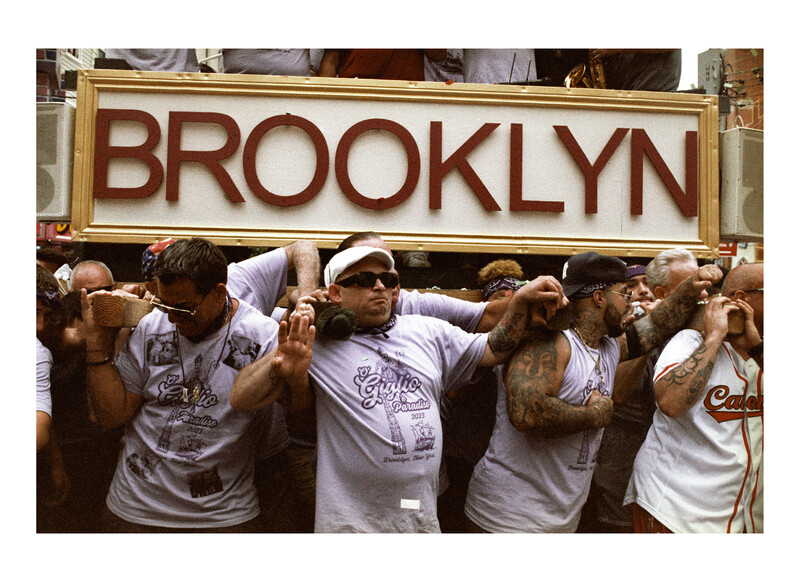 Group of people in white t-shirts holding up a large sign that reads BROOKLYN.