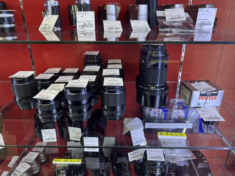Display case of vintage camera lenses and equipment arranged on red shelving.
