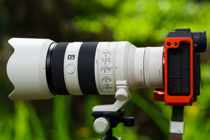 White telephoto lens mounted on red mirrorless camera body with tripod collar and focus ring visible.