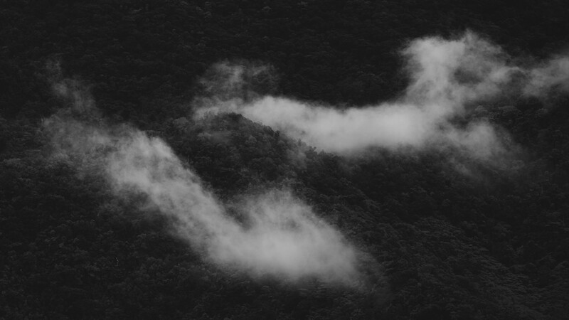 Dramatic black and white photograph of mountainous terrain obscured by swirling mist and clouds.