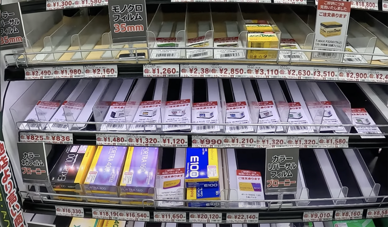 Retail shelf display of camera film rolls and photography accessories with Japanese price tags.