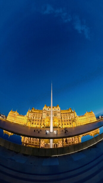 Ornate golden parliament building illuminated at dusk against deep blue sky, shot with fisheye lens distortion.