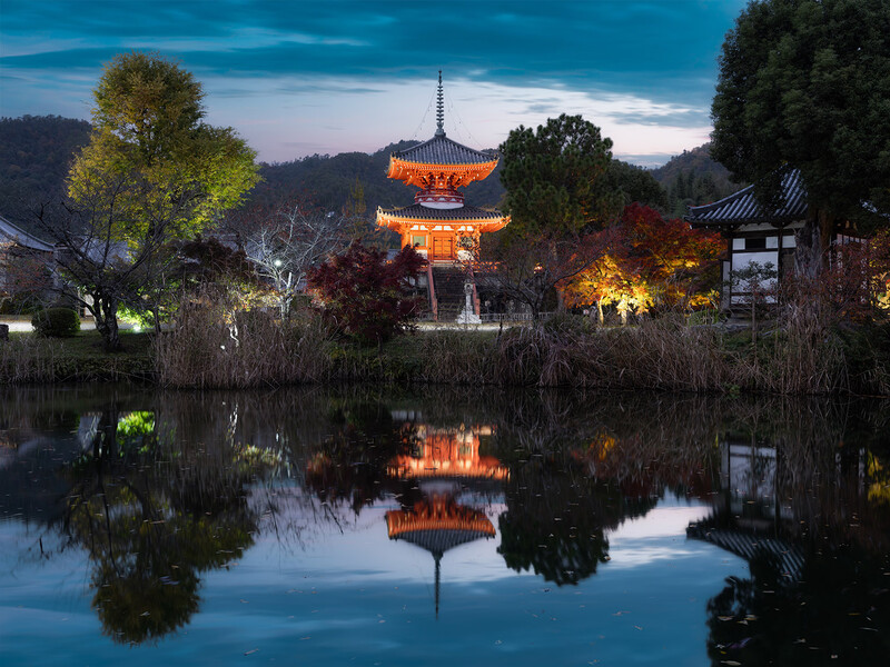 Illuminated Asian pagoda reflected in still water at twilight, surrounded by lit trees.