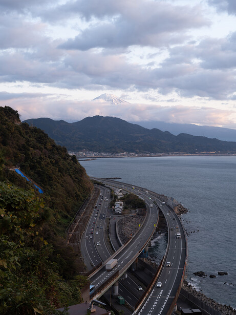 Elevated highway with curved ramps overlooking a coastal bay at dusk with mountains in the distance.