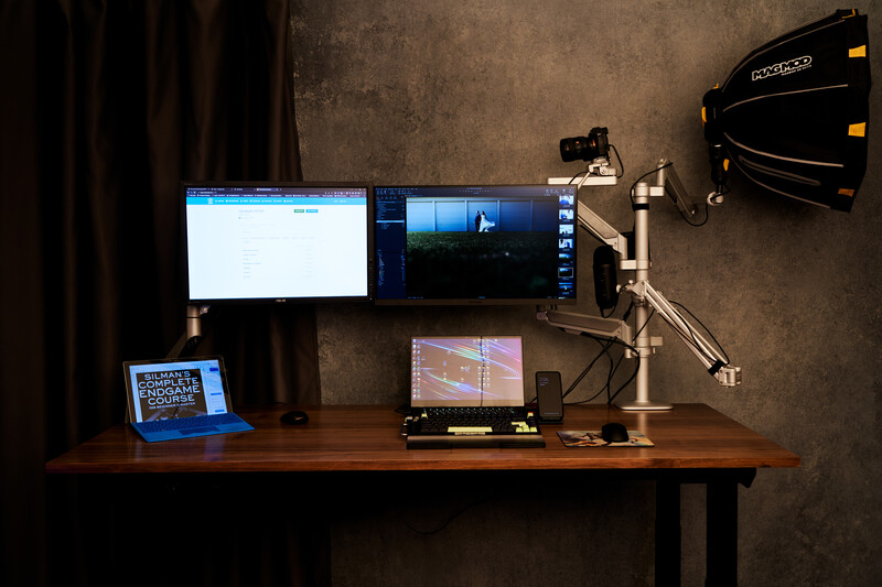 Professional video editing and color grading workstation with dual monitors and lighting equipment mounted overhead.