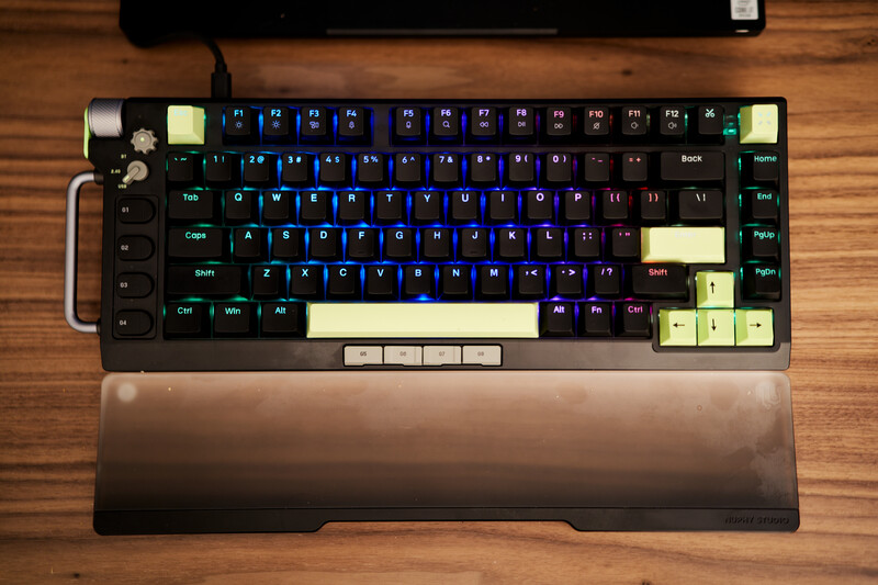 Mechanical keyboard with blue and cream keycaps on wooden surface with wrist rest.