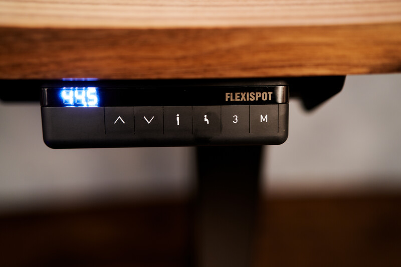 Close-up of a Flexispot monitor arm control panel with adjustment buttons and a blue LED display.