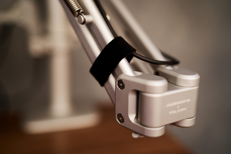 Close-up of a camera microphone mounted on a boom arm with a shock mount and cable attached.