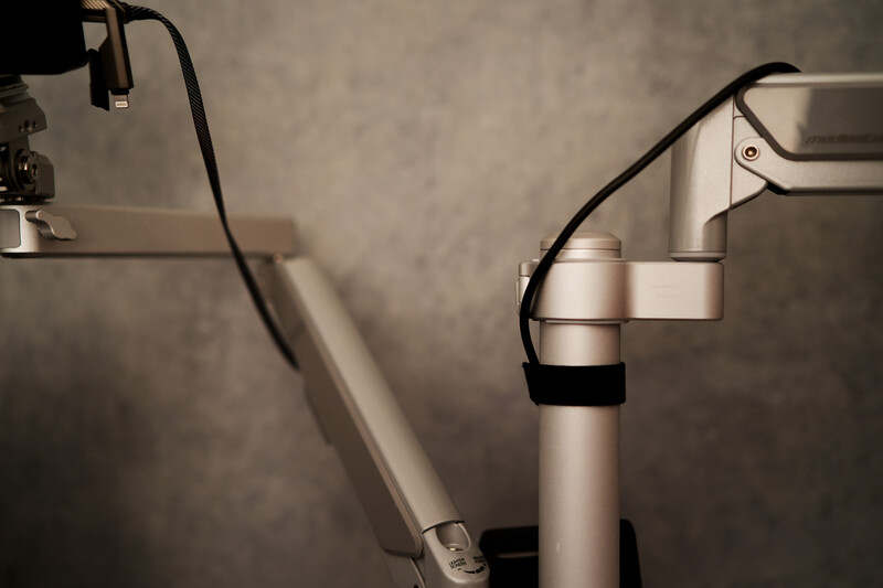 Professional studio microphone mounted on an articulating arm with shock mount and pop filter against gray wall.