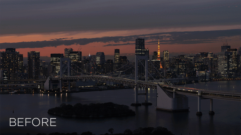 City skyline at dusk with illuminated skyscrapers and a bridge spanning dark water.