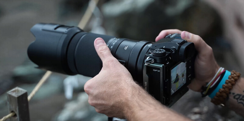 Photographer holding a mirrorless camera with a telephoto lens attached.