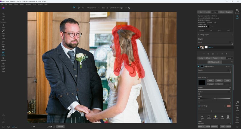 Groom in dark suit and glasses holds hands with bride wearing red veil and white dress during ceremony.