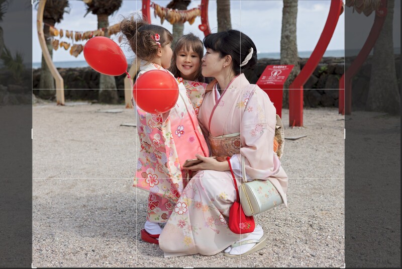 Woman in pink kimono kissing child while holding red lanterns at outdoor festival.