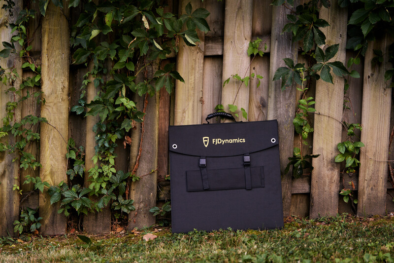Black FDynamics camera bag positioned against weathered wooden fence with climbing ivy.