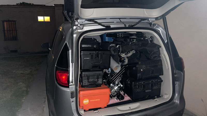 Open hatchback of a silver vehicle revealing an orange toolbox and dark engine compartment components.