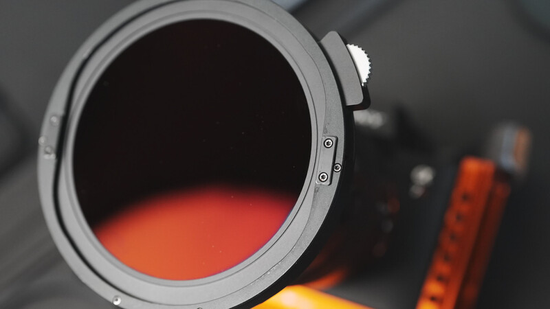 Camera lens barrel with warm orange and red gradient filter effect visible through the glass.