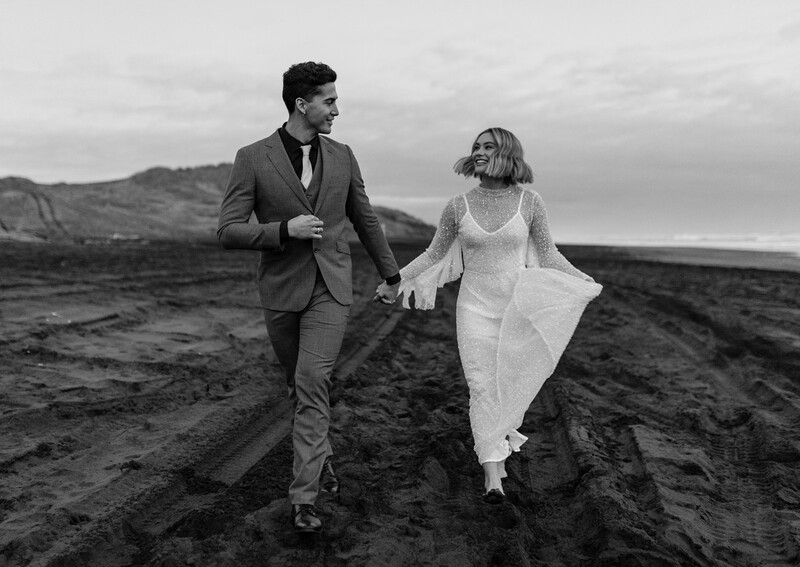 Bride and groom running across dark volcanic landscape in black and white.