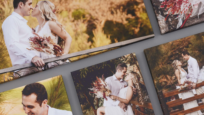Multiple printed wedding photographs arranged on a gray surface, showing a couple in white clothing with burgundy florals in outdoor golden-hour lighting.
