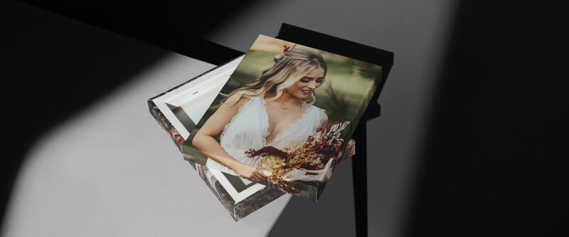 Stack of printed photographs showing a woman in a white top holding dried flowers, displayed at an angle with dramatic side lighting.