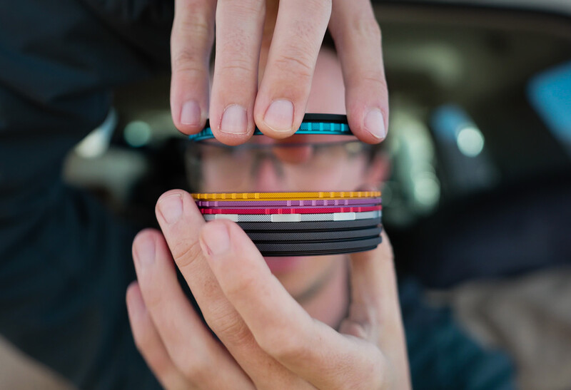 Hands holding colorful camera lens filter strips with rainbow and black bands.