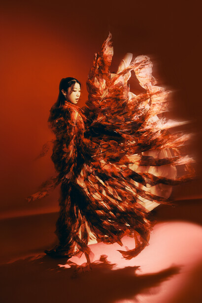 Woman in black outfit with dramatic orange fire-like fabric explosion effect extending from her body.