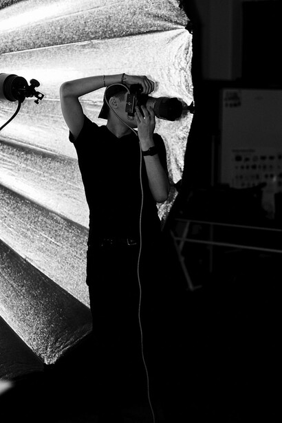 Silhouetted figure adjusting camera settings against a large backlit softbox in a studio.