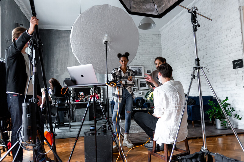 Film or photography production set with crew members operating camera equipment and lighting rigs in a white brick studio.