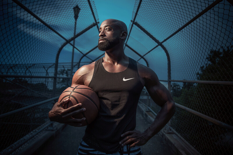 Athletic man holding a basketball in an enclosed court at dusk, wearing Nike gear.