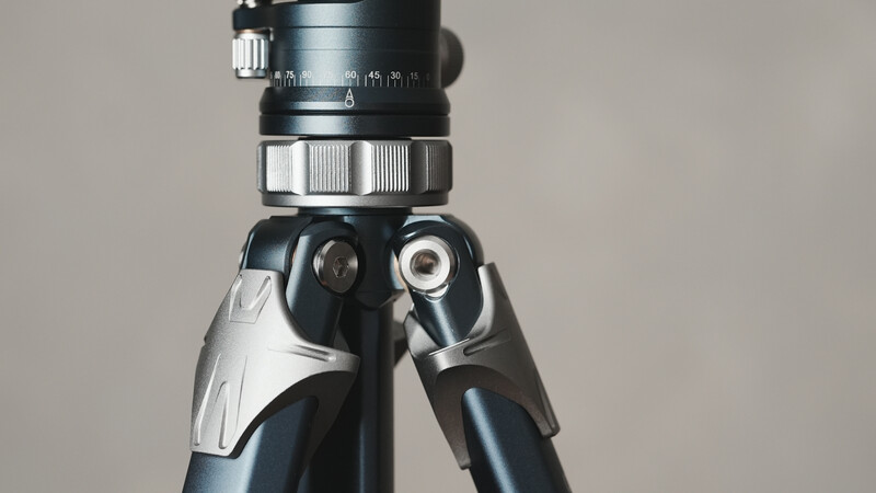 Close-up of a camera tripod head with a telephoto lens mounted on top, showing adjustment knobs and locking mechanisms.