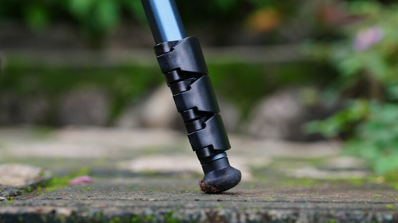 Close-up of a black tripod leg with rubber foot touching wet pavement outdoors.