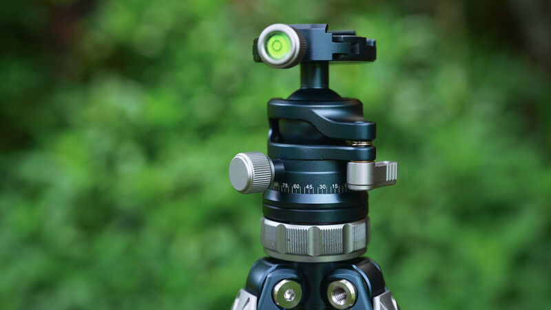 Ball head tripod mount with bubble level and pan-tilt controls against blurred green foliage.