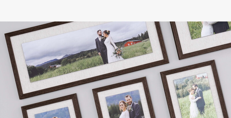 Collection of framed wedding photographs arranged on a white wall, featuring couples in outdoor settings with mountains and fields.