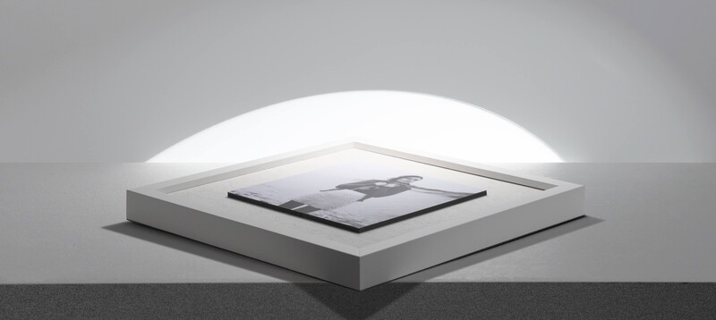Minimalist product display with a tablet device centered on a white stepped platform beneath an arched ceiling light.
